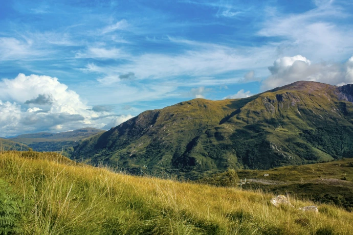 green grass field near mountain under blue sky during daytime